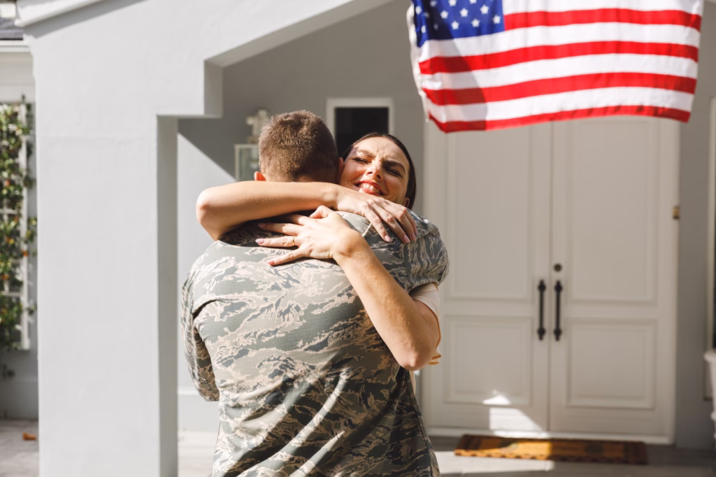 Caucasian male soldier hugging wife outside house decorated with american flag